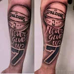 Фото тату на предплечье с изображением баскетбольного мяча Spalding и надписью 'Never Give Up'. Черно-серый рисунок татуировки в реалистичном стиле.