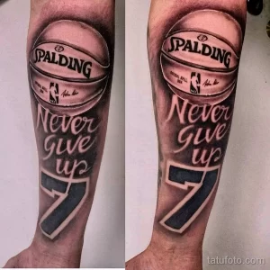 Фото тату на предплечье с изображением баскетбольного мяча Spalding и надписью 'Never Give Up'. Черно-серый рисунок татуировки в реалистичном стиле.