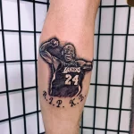 Фото тату на предплечье: портрет Коби Брайанта в форме Lakers с надписью "R.I.P. K.B.". Черно-серые тона, реалистичный стиль, дань уважения.