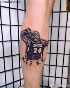 Фото тату на предплечье: портрет Коби Брайанта в форме Lakers с надписью "R.I.P. K.B.". Черно-серые тона, реалистичный стиль, дань уважения.
