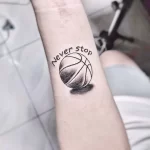 Фото тату небольшого баскетбольного мяча с надписью "Never Stop" на предплечье, выполненного в черно-белой гамме.