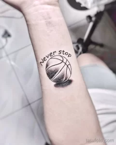 Фото тату небольшого баскетбольного мяча с надписью "Never Stop" на предплечье, выполненного в черно-белой гамме.