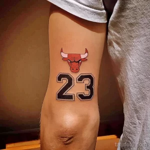 Простое тату с изображением логотипа Chicago Bulls и номера 23. Минималистичный дизайн на предплечье.