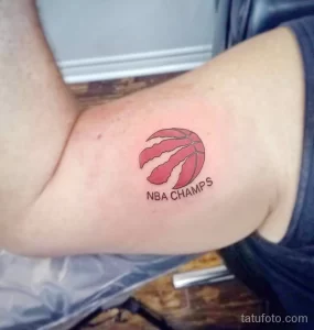 Фото татуировки с изображением логотипа баскетбольной команды Toronto Raptors и надписью "NBA CHAMPS" на руке.