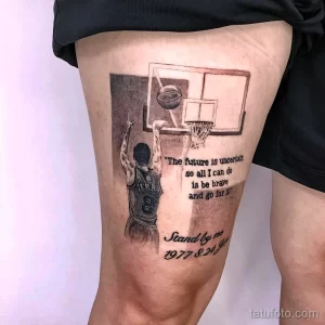 Фото реалистичной татуировки на бедре, изображающей Коби Брайанта в баскетбольном прыжке, с цитатой и датами рождения и смерти. Детальный рисунок татуировки.