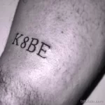Черно-белое фото минималистичной татуировки с надписью 'K8BE' на предплечье, посвященной легенде баскетбола Коби Брайанту. Изящный рисунок татуировки.