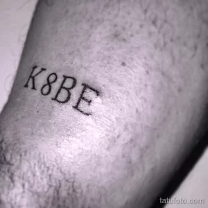 Черно-белое фото минималистичной татуировки с надписью 'K8BE' на предплечье, посвященной легенде баскетбола Коби Брайанту. Изящный рисунок татуировки.