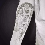 Фото тату на руке с изображением Леброна Джеймса в форме Los Angeles Lakers. Черно-белая татуировка в реалистичном стиле с детальной проработкой лица и формы.