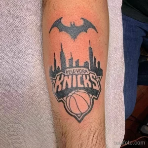 Фото тату на руке, сочетающее логотип баскетбольной команды New York Knicks с силуэтом Бэтмена и изображением небоскребов Нью-Йорка. Черно-белая татуировка в стиле графики.