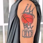 Фото татуировки баскетбольного мяча с короной и надписью 'Ball Don't Lie', выполненной в черно-серых тонах на плече.