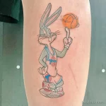 Фото татуировки с изображением Багза Банни из Space Jam, держащего баскетбольный мяч. Яркие цвета, мультяшный стиль, дань уважения культовому фильму.