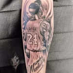 Фото тату реалистичного портрета Коби Брайанта в форме Lakers с надписью 'Mamba Mentality' на предплечье. Детализированный рисунок в черно-серых тонах.