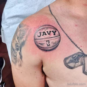 Фото тату с изображением баскетбольного мяча с надписью "JAVY". Реалистичный стиль, детализированный рисунок на плече.