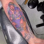 Фото тату на руке, изображающее баскетболиста Коби Брайанта в форме Lakers, держащего мяч. Яркий, цветной рисунок татуировки с надписью "Mamba Mentality".