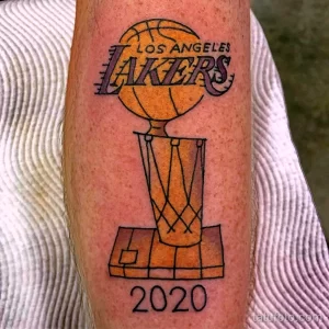 Фото тату с изображением кубка NBA команды Los Angeles Lakers с надписью 2020 года на предплечье. Черно-белый рисунок татуировки.