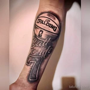 Фото тату на руке: баскетбольный мяч Spalding с надписью "Ball is life" и номером 7. Черно-серый рисунок татуировки в стиле реализм.