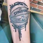 Фото тату с изображением баскетбольного мяча Spalding, из которого стекают капли краски. Черно-серый стиль, динамичный дизайн.