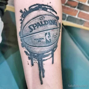 Фото тату с изображением баскетбольного мяча Spalding, из которого стекают капли краски. Черно-серый стиль, динамичный дизайн.