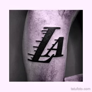 Черно-белое фото тату с логотипом LA Lakers на икре. Простой, но стильный рисунок татуировки для фанатов баскетбола.