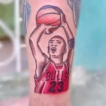Фото тату на руке с изображением Майкла Джордана в красной форме Chicago Bulls. Рисунок выполнен в ярких цветах с использованием красного, черного и белого.