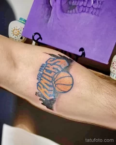 Фото тату на руке с изображением логотипа баскетбольной команды New York Knicks, выполненное в ярких цветах с использованием теней.