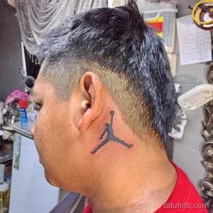 Фото минималистичной татуировки с изображением логотипа Air Jordan, выполненной черным цветом на затылке мужчины.