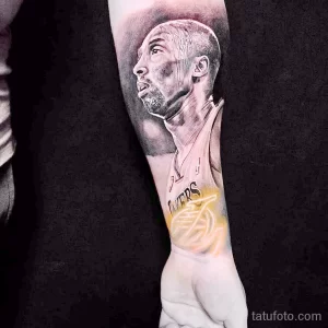 Фото тату на руке с изображением Коби Брайанта в профиль и логотипом Los Angeles Lakers. Черно-белая гамма и детализированная проработка.