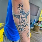 Фото тату Коби Брайанта в форме Lakers с короной над головой и номером 24. Черно-белый рисунок на руке.