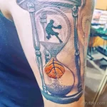 Фото тату песочные часы с силуэтом баскетболиста, играющего в мяч. Черно-серый рисунок на предплечье, символизирующий течение времени.