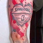 Фото татуировки на руке с изображением баскетбольного мяча Spalding в форме сердца, украшенного брызгами краски. Оригинальный и стильный дизайн.