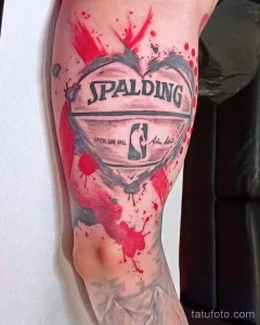 Фото татуировки на руке с изображением баскетбольного мяча Spalding в форме сердца, украшенного брызгами краски. Оригинальный и стильный дизайн.