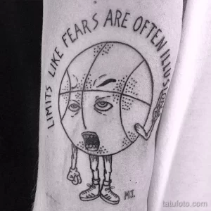 Фото тату баскетбольного мяча с лицом и надписью "Limits like fears are often illusions" на руке.