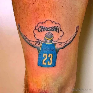 Фото тату на ноге с изображением Леброна Джеймса в форме Cleveland Cavaliers с надписью 'CHOSEN' над головой. Рисунок выполнен в ярких цветах с использованием черного контура.