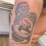 Фото тату на ноге с изображением змеи, обвивающей баскетбольный мяч. Детализированный рисунок в черно-белом цвете, выполненный в стиле реализм.