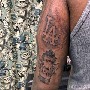 Фото тату на предплечье в стиле чикано с изображением логотипа LA Dodgers, баллончика с краской и надписи "Davon's Secret Stuff". Черно-белый рисунок с использованием теней и текстур.