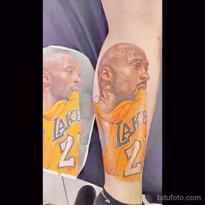 Фото татуировки с изображением Коби Брайанта в форме команды Lakers, выполненной в реалистичном стиле с высокой детализацией и яркими цветами.