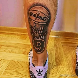 Фото тату на ноге с изображением баскетбольного мяча и надписью 'Ball is life'. Черно-белый рисунок в реалистичном стиле.