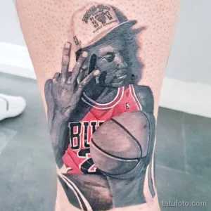 Фото тату на ноге с изображением Майкла Джордана в форме Chicago Bulls, держащего баскетбольный мяч. Детализированный портрет и кепка с надписью.