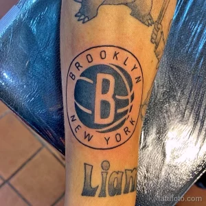 Фото тату на руке: логотип баскетбольной команды Brooklyn Nets, выполненный в черно-белой гамме.
