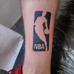 Фото тату на ноге с изображением логотипа NBA в черно-белом цвете. Минималистичный и лаконичный дизайн.
