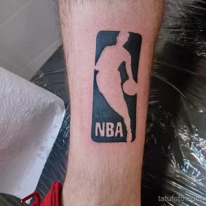 Фото тату на ноге с изображением логотипа NBA в черно-белом цвете. Минималистичный и лаконичный дизайн.