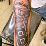 Черно-белое фото тату на руке с изображением баскетбольного мяча Spalding, надписи 'Ball is life' и номера 8 в баскетбольной форме.