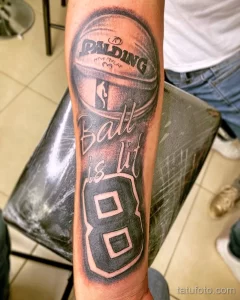 Черно-белое фото тату на руке с изображением баскетбольного мяча Spalding, надписи 'Ball is life' и номера 8 в баскетбольной форме.