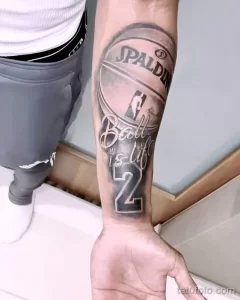 Фото татуировки баскетбольного мяча Spalding с надписью 'Ball is Life' и номером 2. Черно-серый рисунок на руке.