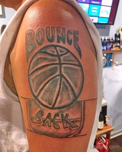 Фото тату с изображением баскетбольного мяча и надписью "Bounce Back". Черно-серый рисунок на предплечье.