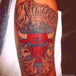 Фото тату на руке с изображением головы быка, символа Chicago Bulls, на фоне городского пейзажа Чикаго. Яркий и детализированный рисунок татуировки.