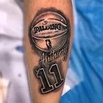Фото татуировки на предплечье с изображением баскетбольного мяча Spalding и надписью 'Anthony 11'. Стильный и персонализированный дизайн.