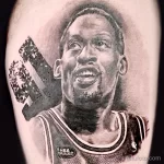 Фото тату на предплечье с реалистичным портретом Денниса Родмана в форме игрока NBA. Рисунок татуировки выполнен в черно-серых тонах.