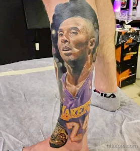 Фото тату с реалистичным портретом Коби Брайанта в форме игрока Lakers на предплечье. Детализированный рисунок татуировки выполнен в черно-серых тонах.