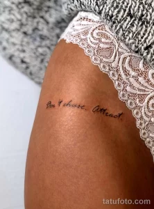 Фото тату с надписью "Don't chase. Attract." на бедре. Тонкие линии и минималистичный дизайн.